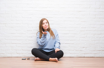 Canvas Print - young adult woman sitting on the floor in autumn over white brick wall looking at the camera blowing