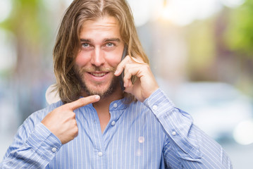 Poster - Young handsome man with long hair over isolated background talking on the phone very happy pointing with hand and finger