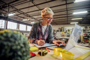 middle age beautiful smiling female engineer with glasses working on projects in her workshop.table 