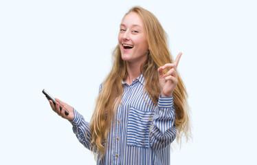 Poster - Blonde teenager woman using smartphone surprised with an idea or question pointing finger with happy face, number one