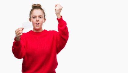 Wall Mural - Young blonde woman holding advertising card annoyed and frustrated shouting with anger, crazy and yelling with raised hand, anger concept