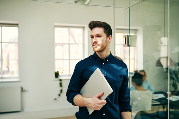 Confident young businessman carrying a laptop in an office