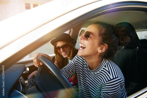 Carefree young friends driving together in a car laughing Poster Mural XXL