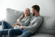 © fizkes - Loving couple hugging holding hands relaxing on cozy couch, smiling boyfriend and girlfriend looking at each other embracing at sofa, young lovers resting enjoying weekend at home together