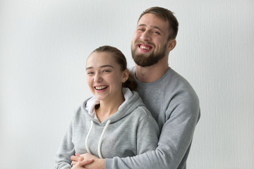 Portrait of smiling millennial couple looking at camera hugging laughing, boyfriend and girlfriend embracing in newly bought own apartment, happy man hold excited woman in arms at home