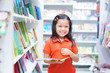 © kornnphoto - Asian children or kid girl red shirt happy smile and shopping or choose tale or story book and read on bookshelf in bookstore or library room at kindergarten school or nursery for learn and study