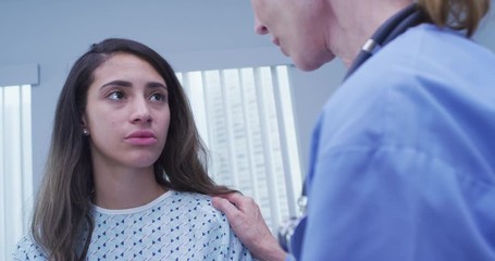 Wall Mural - Mid aged nurse comforts young latina patient wearing hospital gown