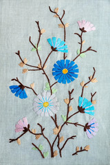 Wall Mural - Beautiful  handmade folk embroidery of pink and blue flowers and buds, brown stems and green leaves on grey linen fabric background. Floral delicate embroider in satin-stitch