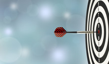Close-up Dart Arrow Hitting On Target Center On Bullseye In Wooden Dartboard With Blurred Blue Lights Bokeh Copy Space Background, Perfection Goal Success, Symbol Of Aim And Achievement