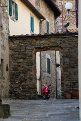 Wall Mural - Red motorbike standing in an arch lining an alley in Cortona, Italy