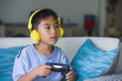 © TheVisualsYouNeed - oung hispanic little kid excited and happy playing video game online with headphones holding controller enjoying having fun sitting on couch in child gaming addiction
