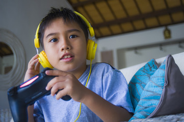 Wall Mural - young Latin little child excited and happy playing video game online with headphones holding controller having fun sitting on couch in kid gaming addiction