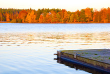 A Scenic Wooden Pier At A Lake With Colorful Red And Orange Forest In The Background During A Lovely Autumn Day, The Perfect Place To Fish And Relax.