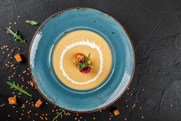 Cream soup of lentils with breadcrumbs on plate. Top view on a dark grey stone surface. Healthy vegan food