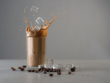 Iced Coffee Splash With Ice Cubes And Beans Against Grey Concrete
