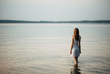 woman in summer dress standing on seashore and looking at horizon. young beautiful girl standing in 