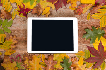 Autumn concept, tablet with empty screen for adding text surrounded with autumn leaves 