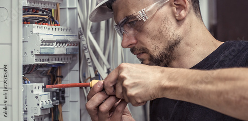 Fotomural a male electrician works in a switchboard with an electrical connecting cable