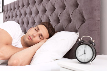 Poster - Young man sleeping in bed and alarm clock on nightstand at home