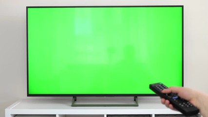 Watching tv with green screen at home interior. Push buttons on remote. Changing channels on television