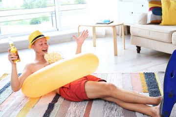 Sticker - Shirtless man with inflatable ring, drink and popcorn wearing flippers on floor at home