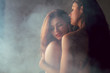 Two caucasian women in lingerie pose together on a chair