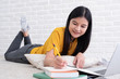 © weedezign - Asian woman lying on carpet and writing on notebook and learning on laptop with relax emotion at home,work at home concept.online learning.
