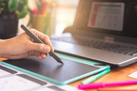 graphic designer hand working with stylus pen and laptop computer for creative project.