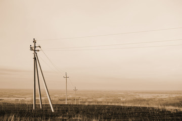 Atmospheric landscape with power lines in field under sky in sepia tones. Background image of electric pillars with copy space. Wires of high voltage above ground. Electricity industry in monochrome.