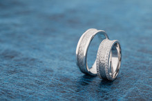 Two Textured Silver Wedding Rings On Blue Background
