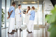 © Maskot - Full length of multi-ethnic healthcare team discussing while standing at lobby in hospital