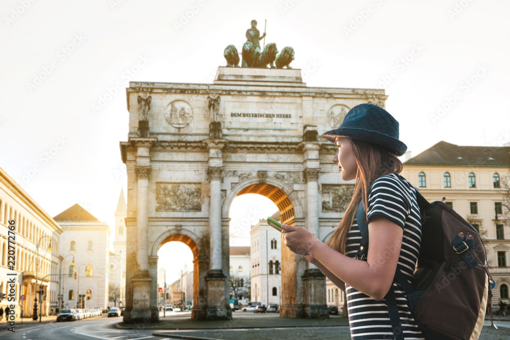 A tourist girl with a backpack looks sights in Munich in Germany. Passes by the triumphal arch. - obrazy, fototapety, plakaty 