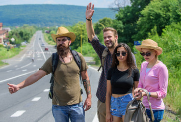 Wall Mural - Friends hitchhikers travelling summer sunny day. Travellers try to stop car. Company friends travelers hitchhiking at edge road nature background. Begin great adventure in your life with hitchhiking