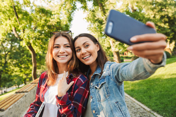 Sticker - Beautiful ladies students walking in the park take a selfie by mobile phone.