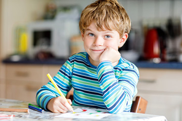 Portrait of cute healthy happy school kid boy at home making homework. Little child writing with colorful pencils, indoors. Elementary school and education. Kid learning writing letters and numbers