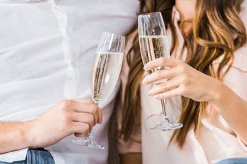 Wall Mural - cropped shot of couple clinking glasses of champagne on sofa at new home