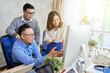 © DragonImages - Group of young Asian men and woman standing at desk in office watching computer and having friendly discussion