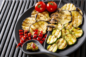 Grilled vegetables: eggplant, zucchini, pepper. Skewer with mushrooms. On a black plate and a black background.