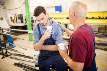 Senior foreman supporting and comforting his upset young subordinate during coffee-break in workshop