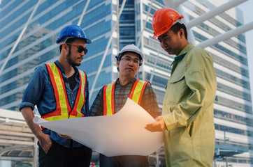 group of engineer, technician and architect with safety helmet planning about building plan with blueprint in modern city building background, construction site, business, industry and worker concept