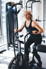 Wall Mural - Young woman riding on an air bike at the gym.