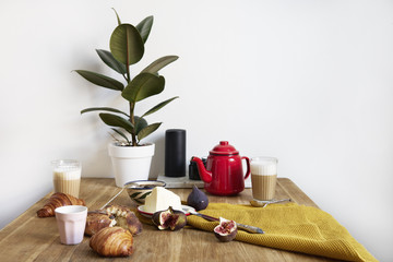 Breakfast with croissants, figs, coffee on wooden background, red tea pot, ceramics dishes