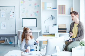 Two young creative colleagues in casualwear discussing new ideas or plans at meeting in office