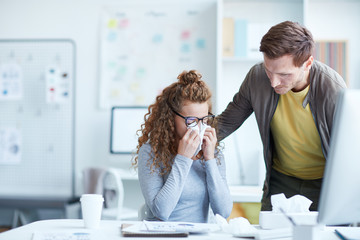 Young businessman leaning over his upset female colleague crying and wiping her tears with paper tissue