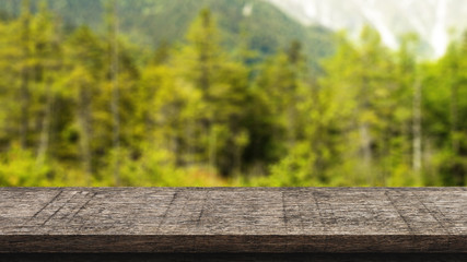 Empty wooden table isolated on blurred green nature background. For your product placement or montage with focus to the table top in the foreground. Empty dark wooden shelf