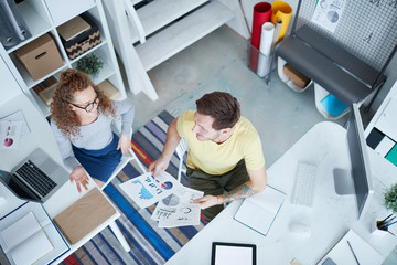 Top view of two young casual economists discussing some papers and consulting in office