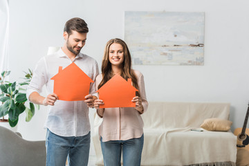 Poster - portrait of smiling couple showing paper houses in hands at new home