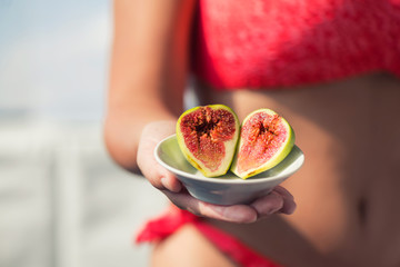 Woman's hand holding a two ripe sliced figs. Female in the bright bikini with fresh sweet exotic fruit at the hot summer time