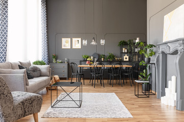 Black table on rug near grey sofa and armchair in spacious interior with chairs and poster. Real photo