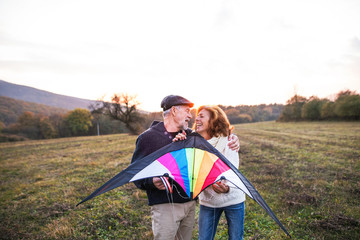 Wall Mural - Senior man and a woman holding a kite in an autumn nature at sunset.